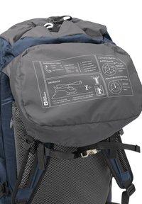 Sac à dos avec un panneau d'information d'urgence gris affichant les signaux de secours alpins, les numéros d'appel d'urgence et les instructions de sécurité pour l'atterrissage des hélicoptères.