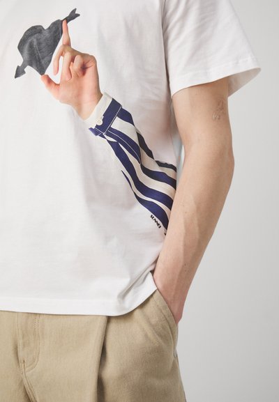 Tricou alb din bumbac, cu un grafic care ilustrează o mână făcând un gest, având un design cu mâneci în dungi albastre și albe pe lateral.