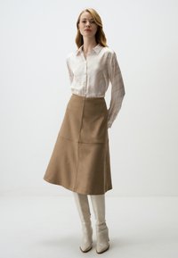 Blouse rayée de couleur claire avec un devant à boutons ; jupe beige mi-longue avec des coutures en panneau ; bottes blanches brillantes jusqu'aux genoux.
