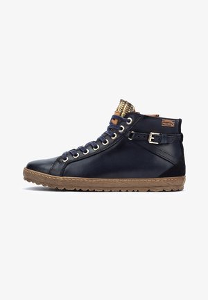 Baskets montantes en cuir bleu marine avec une semelle en caoutchouc beige texturé, présentant des œillets dorés, une sangle sur le côté et une languette à motifs.