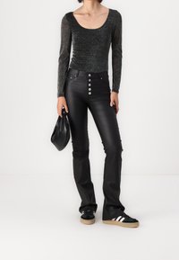 Pantalon évasé en similicuir noir avec bouton argenté à l'avant. Haut à manches longues scintillant dans des tons foncés. Accessoire : petit sac noir. Baskets avec des bandes blanches.