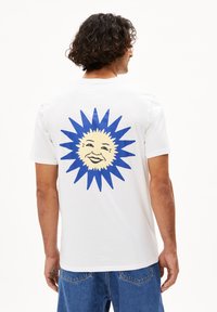 Witte katoenen t-shirt met een blauwe zonafbeelding met een glimlachend gezicht en spitse stralen op de achterkant. Casual fit met korte mouwen.