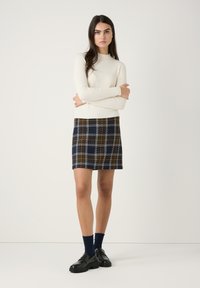 Crème ribbeltrui gecombineerd met een marineblauwe geruite rok met oranje en witte lijnen, afgemaakt met zwarte schoenen en donkerblauwe sokken.