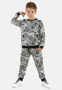 Schwarz-weißer Dinosaurier-Motiv-Sweatshirt und Jogginghose mit elastischen Bündchen, versehen mit Comic-artigen Grafiken und textlichen Akzenten.