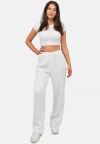 Witte, gestructureerde wijde broek met een elastische tailleband, gecombineerd met een aansluitend wit crop top en witte sneakers.