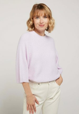 Pull en tricot léger lavande, moelleux, avec un col rond et des manches mi-longues, associé à un pantalon crème.