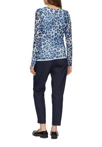 Langemouw top met een blauw luipaardprint, gemaakt van doorschijnende stof, gecombineerd met marineblauwe tapered broek en zwarte instappers.