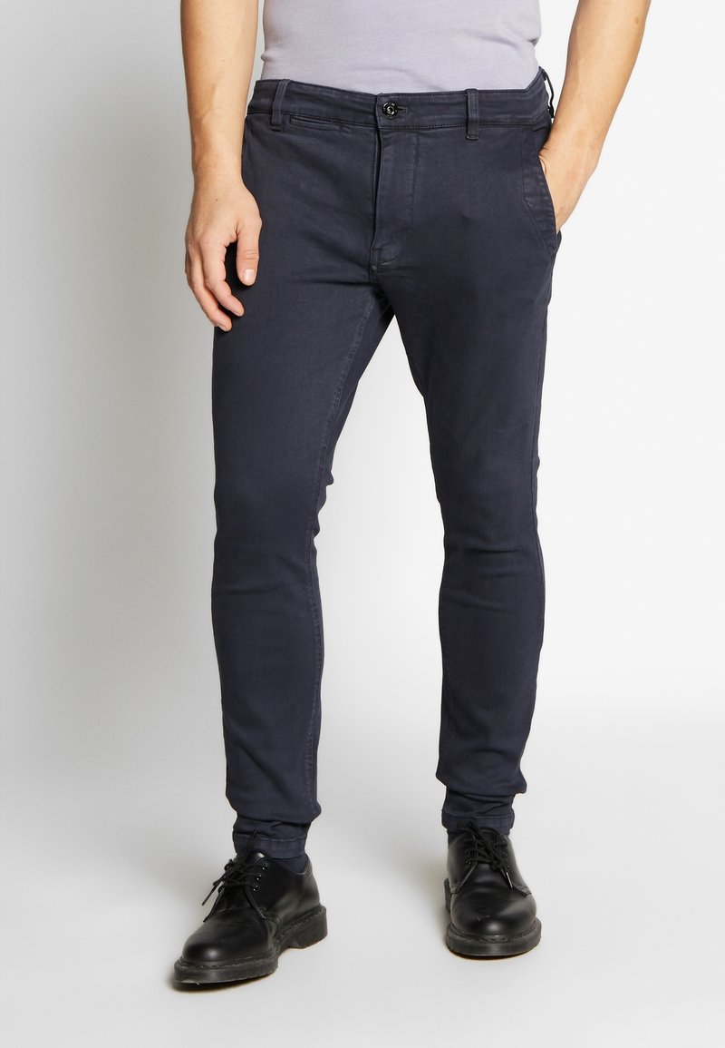 Pantalon ajusté bleu marine en tissu mélangé coton, doté d'une fermeture à bouton, de poches avant, et d'une texture lisse avec peu de détails.