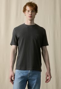 Tricou negru închis cu guler rotund, cu mâneci scurte, textură moale, branding subtil pe piept, asociat cu blugi albastru deschis.