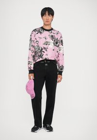 Felpa rosa con motivi floreali e uccelli neri, pantaloni neri e un cappellino rosa con testo. Le sneakers completano l'outfit.