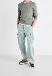 Grå stickad tröja, ljusblå cargobyxor med sidofickor, och flerfärgade sportskor. Slät textur, avslappnad passform, avslappnad stil.