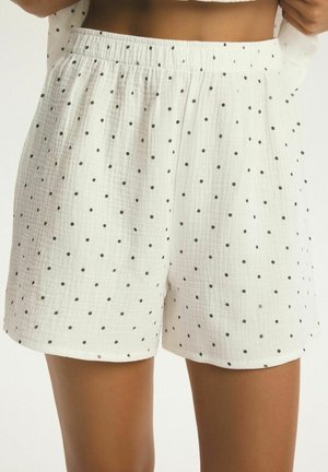 Białe szorty z fakturowanej tkaniny w małe czarne groszki, noszone przez osobę trzymającą pasujący top.