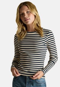 Námornícka a krémová pruhovaná dlhá košeľa s rebrovanou textúrou a okrúhlym výstrihom, kombinovaná s denimovými džínmi.