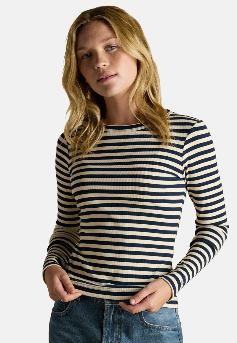 Námornícka a krémová pruhovaná dlhá košeľa s rebrovanou textúrou a okrúhlym výstrihom, kombinovaná s denimovými džínmi.