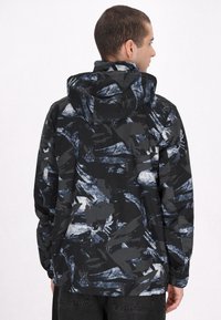 Blå-sorte mønstrede jakke med hætte, der har en blanding af abstrakte penselstræk-designs, lavet af letvægtsmateriale.