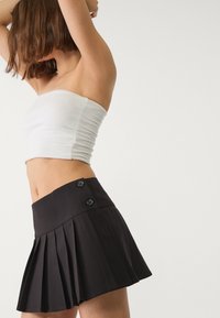 Mini jupe plissée noire avec une taille ajustée, ornée de deux boutons. Le tissu semble lisse avec un design structuré.