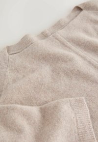 Lys beige strikket sweater med en blød tekstur, prydet med ribbede kanter og en rund halsudskæring, vist fladt mod en neutral baggrund.