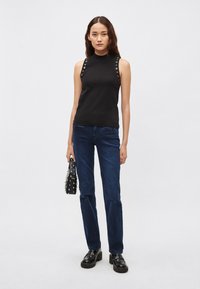 Must mustriga topp hõbedaste silmusriputistega õlgadel, kombineeritud tumeliste siniste teksade ja mustade platvormkingadega, hoides käes naelutatud käekotti.