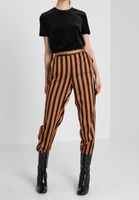 Svart sammetstopp med kort ärm kombinerat med högmidjade, randiga byxor i orange och svart. Glansiga svarta ankelskor fulländar outfiten.