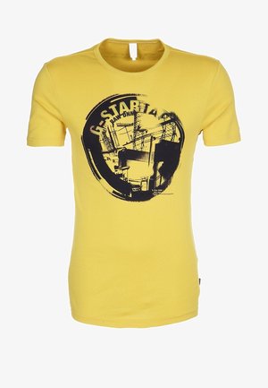 Yellow short-sleeve t-shirt with black circular graphic of industrial structures and partial "G-STAR RAW" text on the front.