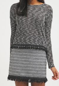 Suéter de patrón en blanco y negro con mangas largas, que presenta flecos en el dobladillo. Combinado con una falda a rayas en blanco y negro con flecos.
