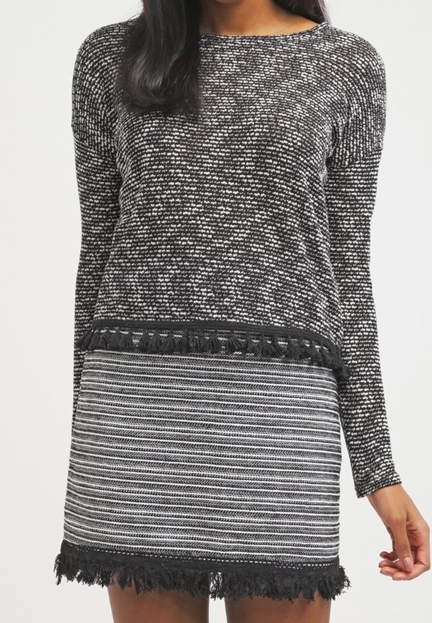 Suéter de patrón en blanco y negro con mangas largas, que presenta flecos en el dobladillo. Combinado con una falda a rayas en blanco y negro con flecos.
