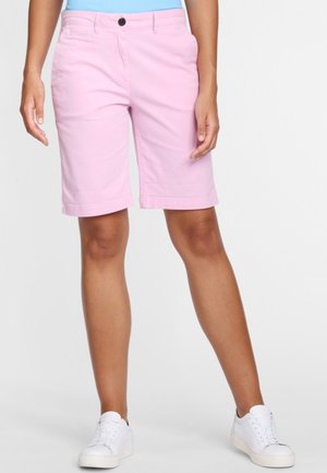 Persona con pantalones cortos rosas hasta la rodilla, zapatillas blancas y una camiseta azul clara, con las manos relajadas a los lados.