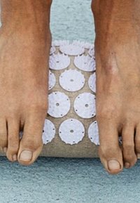 Rouleau de yoga pour les pieds avec une surface texturée beige clair, comportant des disques circulaires blancs disposés en motif. Les pieds sont posés sur le rouleau.