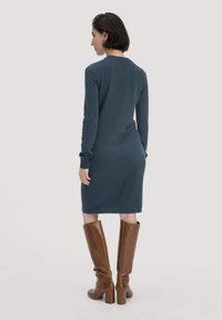 Abito in maglia blu-grigio, di media lunghezza, con maniche lunghe e una silhouette aderente, abbinato a stivali alti in pelle marrone con tacco a blocco.