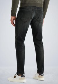Vaqueros de mezclilla negros de corte slim, con un diseño de altura media, dos bolsillos traseros y costuras en contraste, combinados con zapatillas blancas.