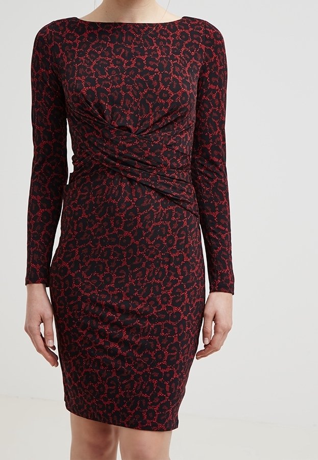 Robe noire à manches longues et longueur genou avec un imprimé léopard abstrait rouge et un détail de tissu froncé à la taille, portée par une personne debout.