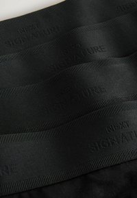 Musta elastinen nauha, jossa on teksturoitu pinta ja kohotettu "SIGNATURE"-teksti. Sen pinta on sileä ja leveys on tasainen koko matkalta.