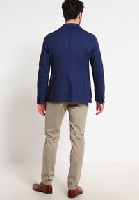 Námořnický blazer vyrobený z texturované látky, s jedním zadním ventilem, slim fit a knoflíkovými manžetami, kombinovaný s khaki kalhotami a hnědými botami.