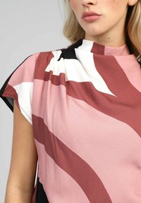 Blouse en satin présentant des motifs abstraits dans des teintes de rose, blanc et noir. Col haut, manches courtes et détail de tissu drapé.