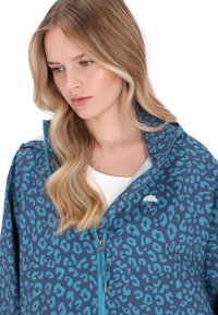 Sininen leopardi-kuvioitu takki, joka on valmistettu kevyestä materiaalista. Takissa on vetoketjukiinnitys ja pieni valkoinen sateenvarjologo rinnassa.