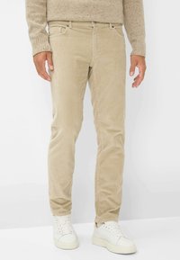 Beige corduroy broek met een rechte pijpdesign. Heeft subtiele verticale ribbels, voorzakken en is gecombineerd met witte sneakers.