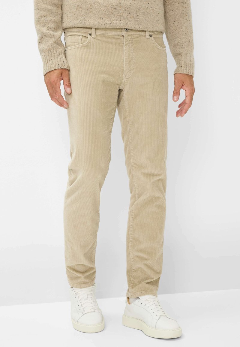 Beige corduroy broek met een rechte pijpdesign. Heeft subtiele verticale ribbels, voorzakken en is gecombineerd met witte sneakers.