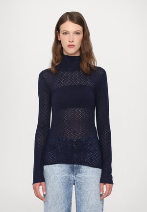 Maglione a maniche lunghe ecollo alto navy con un design a maglia trasparente caratterizzato da motivi a diamante, abbinato a jeans chiari in denim.