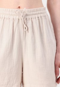 Shorts beige clair en tissu texturé, dotés d'une taille élastique avec cordon de serrage. Design plissé avec une coupe décontractée.
