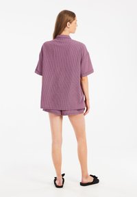 Top a maniche corte, con colletto, in tessuto leggero di un tenue colore viola con un sottile motivo a quadri, abbinato a pantaloni corti. Sandali neri.