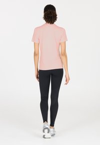 Vaaleanpunainen lyhythihainen urheilupaita, joka on yhdistetty mustiin legginsseihin, joissa on verkkoihin perustuvia yksityiskohtia ja korkea vyötärö. Kengät ovat hopeiset juoksukengät.