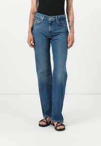 Jean en denim bleu clair avec une coupe droite, présentant une disposition classique à cinq poches et une fermeture à bouton et à zip. Détails de couture plate.