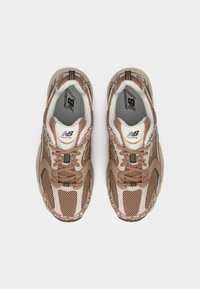 Ζευγάρι καφέ και μπεζ αθλητικά παπούτσια New Balance με σχεδιασμό από δίχτυ και κορδόνια, φωτογραφημένα από πάνω σε λευκό φόντο.