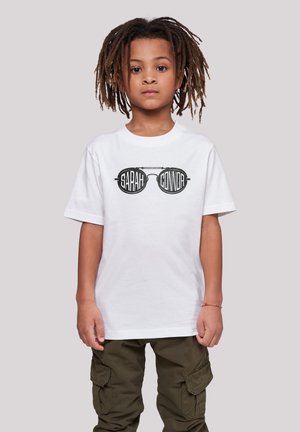 Weißes T-Shirt mit kurzen Ärmeln, das einen grafischen Druck von schwarzen Sonnenbrillen mit den Texten "SARAH" und "CONNOR" zeigt. Olivgrüne Cargo-Hosen.