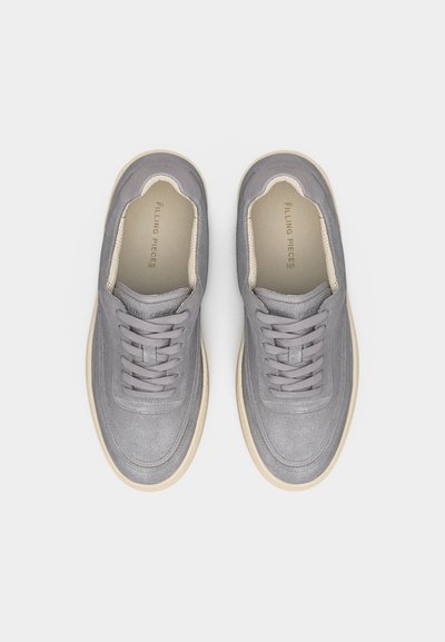 Paire de baskets en daim gris avec semelles et lacets blancs, vues de dessus sur un fond clair, semelles intérieures marquées "FILLING PIECES".