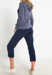 Mörkblå hoodie med dragsko i huvan, åtsittande ärmar och ribbad nederkant. Matchas med korta mörkblå byxor och vita sneakers.