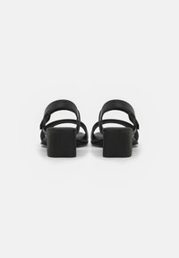 Black heeled sandals featuring a block heel, multiple thin straps, and a smooth leather finish. Back view highlights minimalist design.