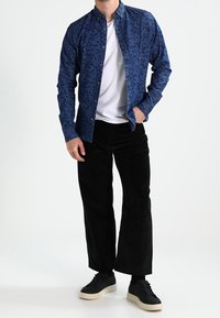 Sininen napillinen kauluspaita lehtikuvioilla, alla valkoinen t-paita, mustat flanellihousut ja mustat tennarit valkoisilla pohjilla.