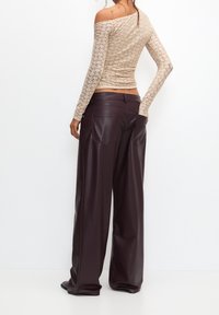 Béžový krajkový top s dlouhým rukávem a off-shoulder designem, kombinovaný s širokými nohavicemi z tmavě burgundské umělé kůže, které mají dvě zadní kapsy.