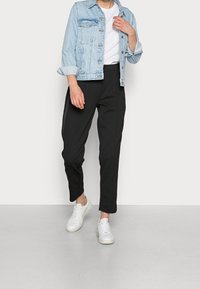 Lichtblauwe denimjas met twee borstzakken, wit t-shirt, zwarte tapse broek en witte sneakers. Eenvoudige, casual outfit.